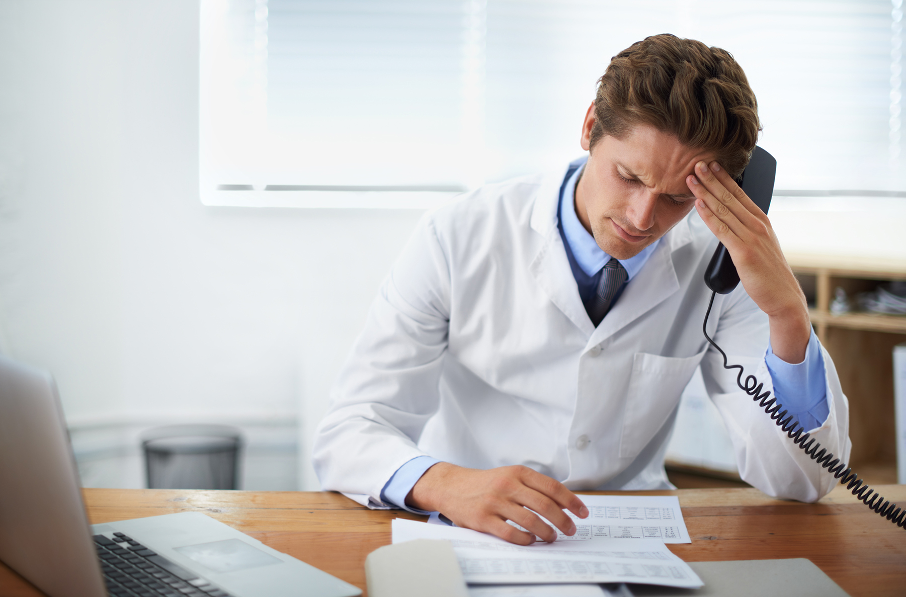 doctor on phone with headache, staring at papers on desk