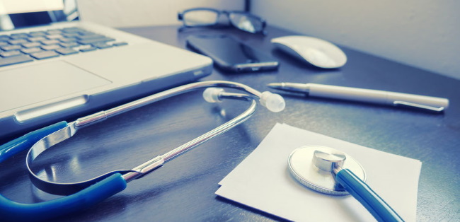 stethoscope and prescription pad on table next to a laptop computer