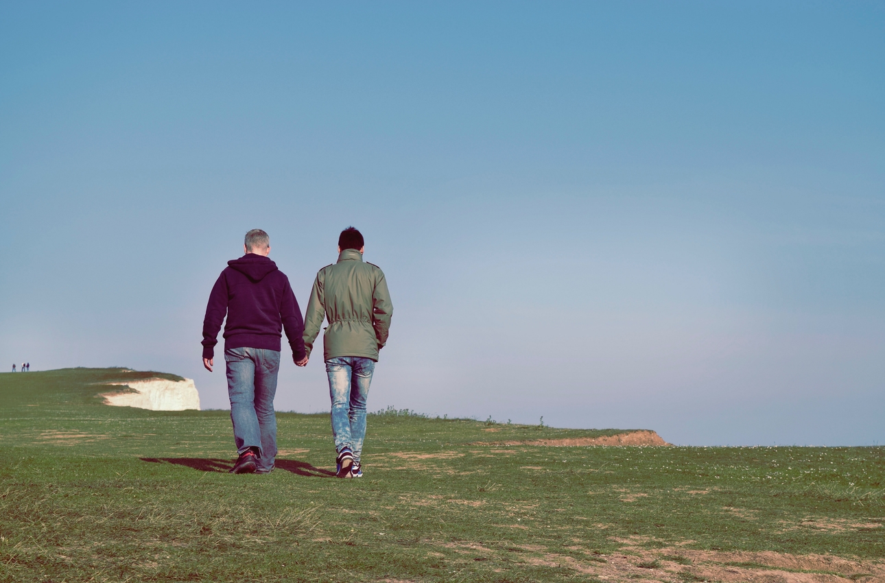 two men holding hand walking in a field